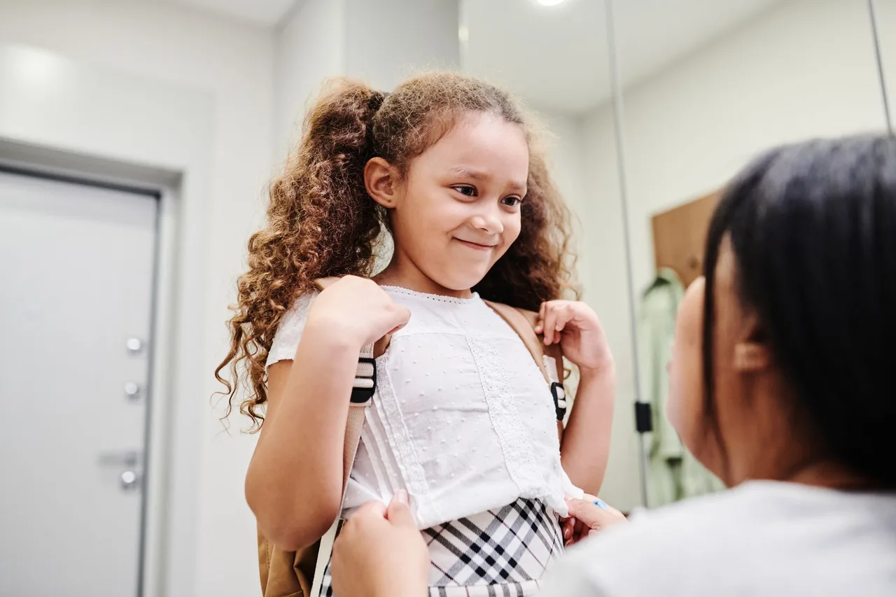 Criança com mochila às costas à saída da escola, à espera dos pais