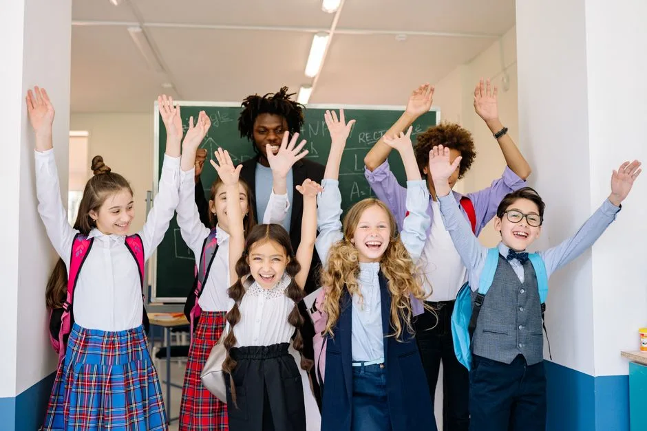 Crianças diversas numa sala de aula inclusiva a levantar o braço para participar