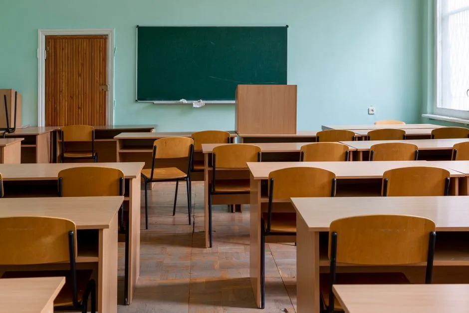 Sala de aula vazia com secretárias e quadro, simbolizando vagas de professores ainda por preencher