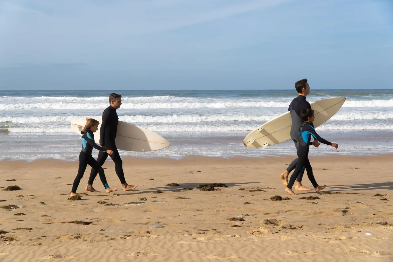 Família a caminhar numa praia portuguesa com pranchas de surf na mão