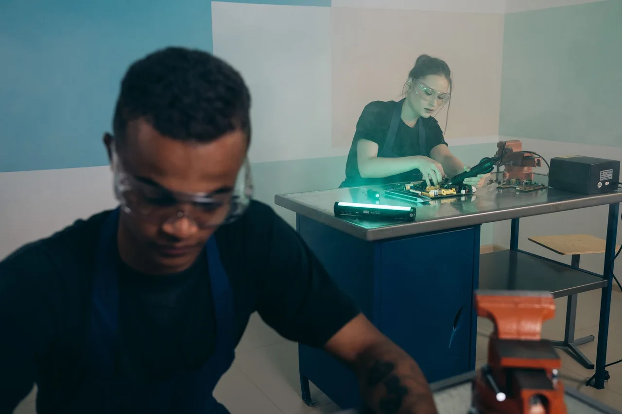 Dois jovens com óculos de proteção a trabalhar numa oficina técnica, representando o ensino profissional