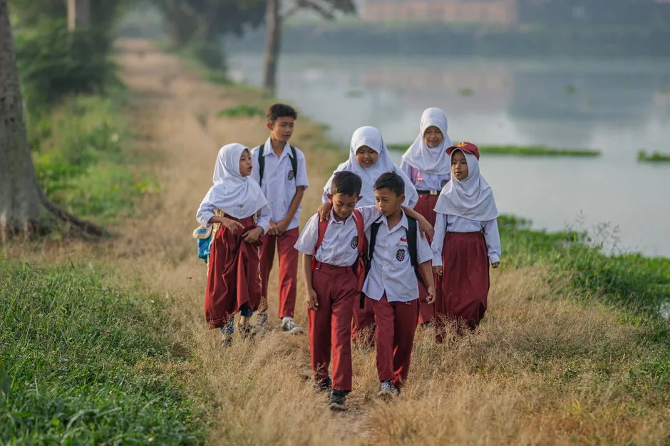 Crianças com uniforme escolar a caminhar por um caminho rural a caminho da escola